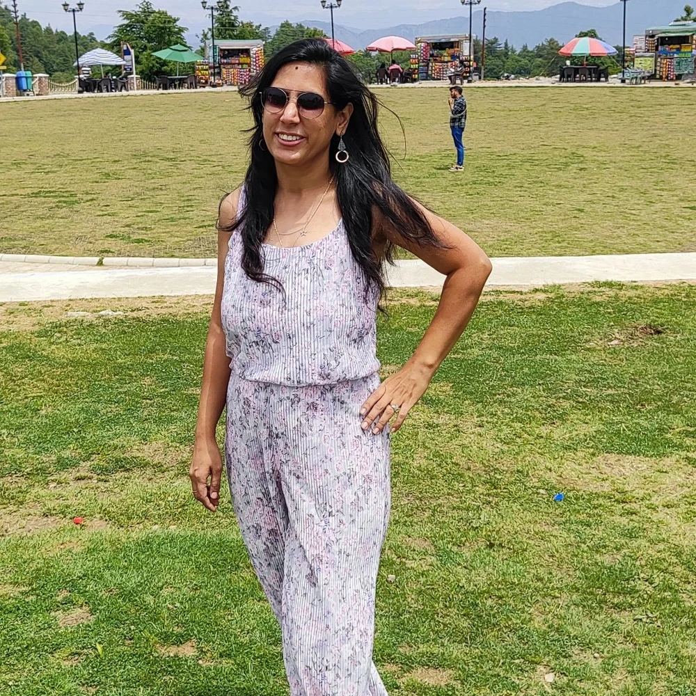Poonam smiling on a hilltop lawn with mountains behind her