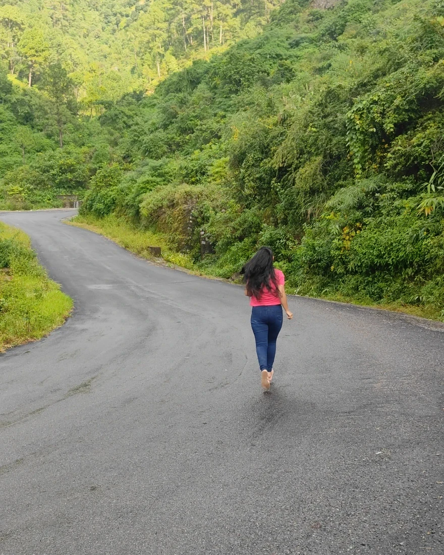 Poonam walking up a winding mountain road through green forest