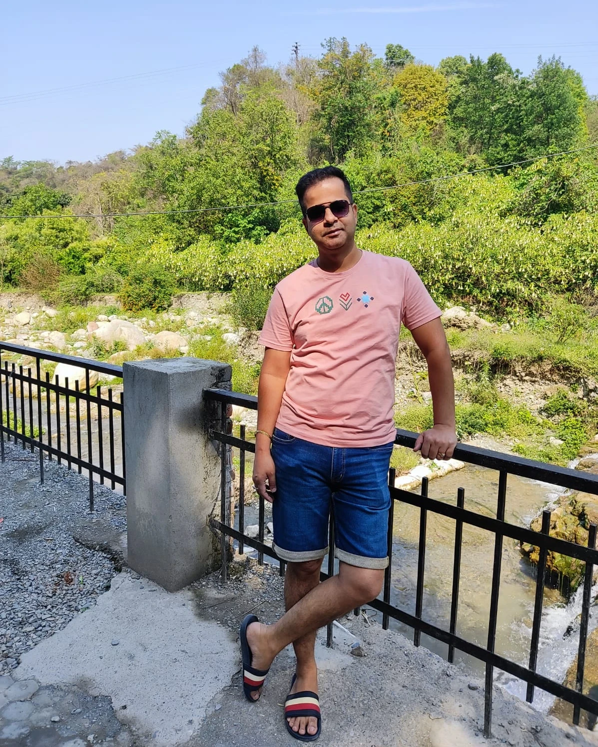 Sunil leaning on a bridge railing above a hill stream